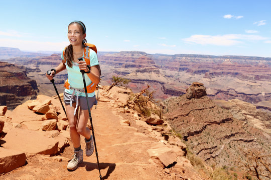 Smiling young female hiker walking on Grand Canyon. Full length of beautiful woman holding hiking poles while climbing rocky mountains. Attractive trekker is enjoying vacation.