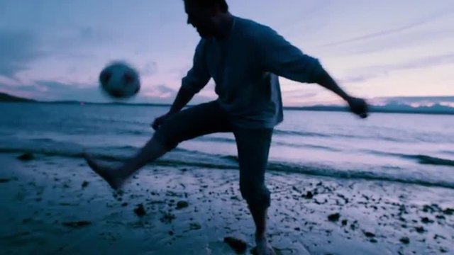 Man  Juggling  Soccer  Ball  Close  Up  on  Seashore  at  Sunset
