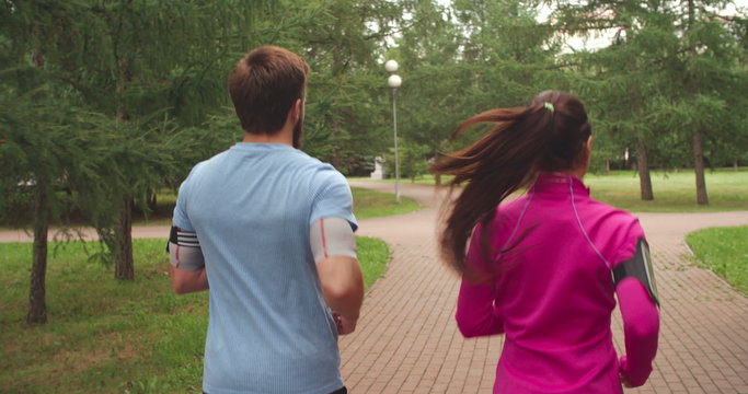 Rear view of young couple jogging through park together
