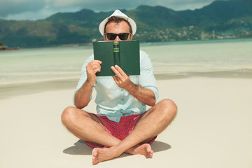 man sitting and hiding behind textbook on the beach