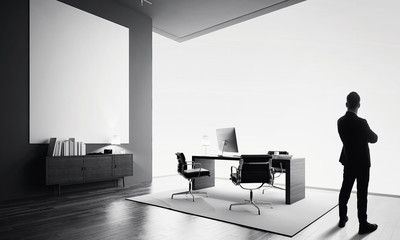 Businessman stands in modern office with one empty canvas. Black and white