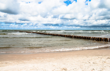 Landscape of beach,  sea with waves, cloudy sky and breakwater.