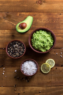 Sauce guacamole an ingredientes - avocado, lemon, salt and pepper on wooden dark background. Vertical