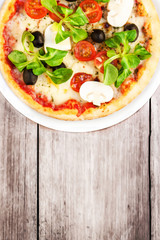 Pizza with fresh vegetables over rustic wooden table top view cl
