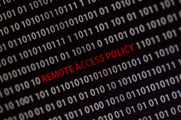 'Remote access policy' text in the middle of the computer screen surrounded by numbers zero and one. Image is taken in a small angle.