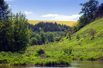 Naklejka na ściany i meble landscape of a river, green grassy hills with trees and sky