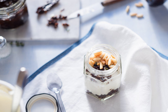 Greek yogurt with roasted pine nuts,  marinated dried tomatoes and thyme in jar. Selective focus.