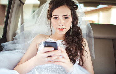 Beautiful bride sitting in car straight with mobile phone hairstyle and bright makeup.