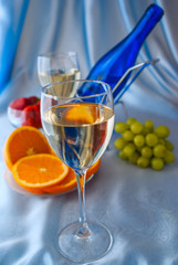 Glass of white wine and blue bottle with oranges and strawberry