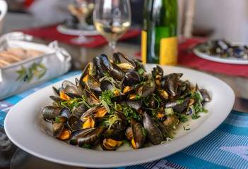 Mussels in a porcelain plate on a table against the background of a bottle of wine
