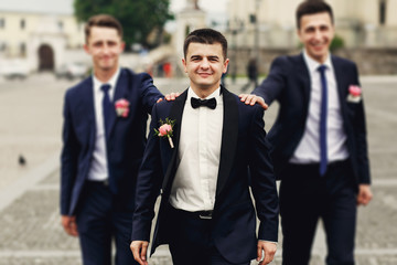 Confident smiling handsome groom in black suit with two groomsma