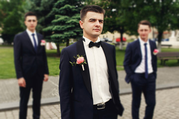 Confident posing handsome groom in black suit with two groomsman