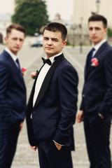 Confident posing handsome groom in black suit with two groomsman