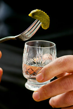 glass of vodka and pickled cucumber on a fork in male hands.