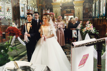 Fototapeta premium Religious blonde bride and handsome groom in crowns at the weddi