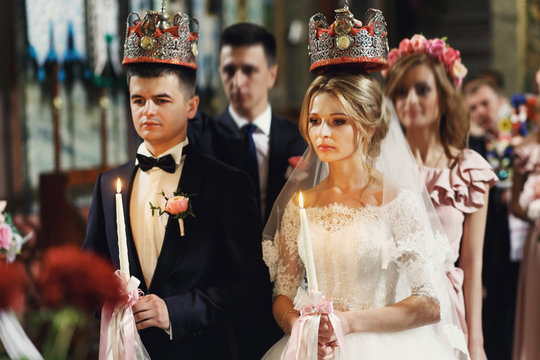 Religious blonde bride and handsome groom in crowns in church at