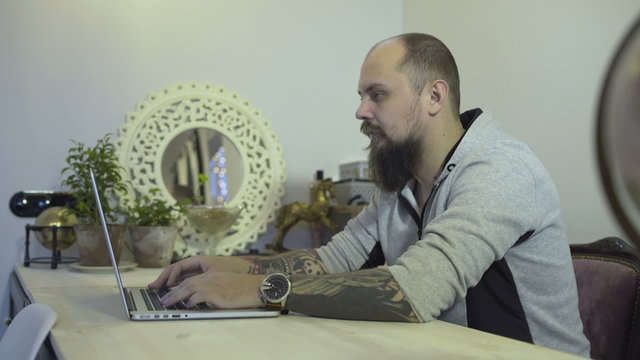 A man with a tattoo on his hand typing on a computer
