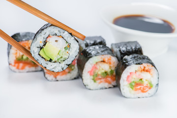 close up of chopsticks taking portion of sushi roll on the table