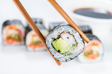 close up of chopsticks taking portion of sushi roll on the table - Powered by Adobe