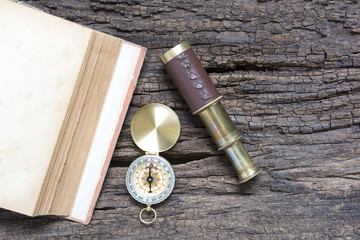 Old book and compass and spyglass on wood