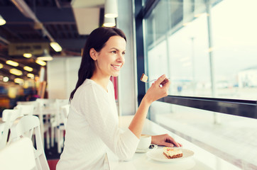 smiling young woman with cake and coffee at cafe