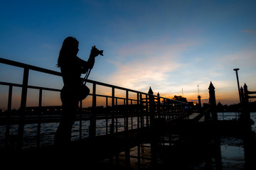 Woman taking a photo with sunset silhouette blur background
