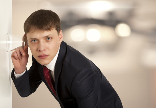 Businessman spying by listening through wall with glass