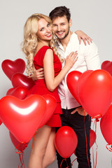 Fototapeta na wymiar Portrait of smiling couple with balloons heart, isolated on grey