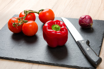 Black cutting board with knife and vegetables, ready for slicing