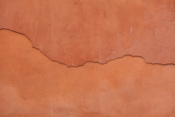 Old terracotta painted stucco wall with cracked plaster. Backgro