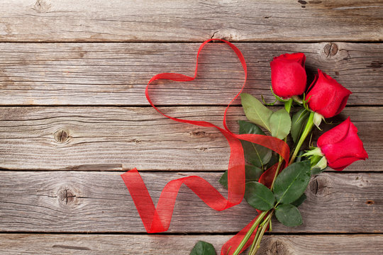 Red roses and heart shape ribbon over wood