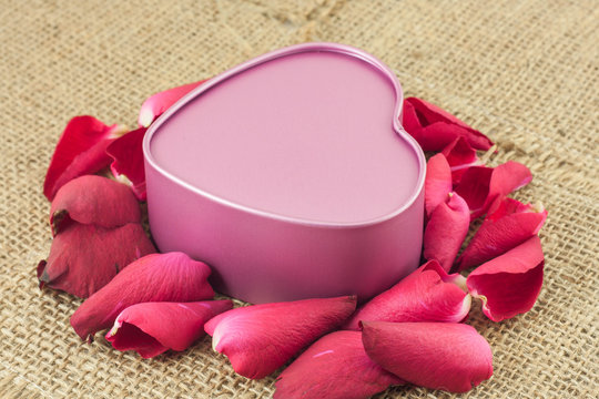 Heart shaped metal box with a red rose is placed on sackcloth.