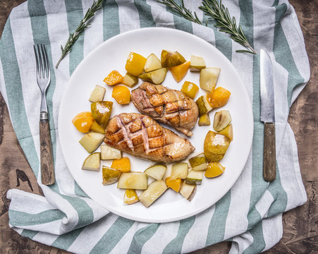 Roast duck breast with pear and peach on a white plate with knife and fork on striped napkin  on wooden rustic background top view close up
