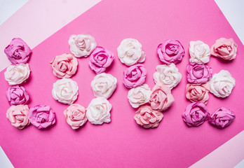 word love made of paper roses, decorations for Valentine's Day  on paper white rustic background top view close up