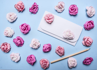 white envelope on a blue background with colorful paper roses and pencil top view close up