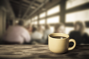 Coffee in cup on wooden table opposite a blurred background. Ton