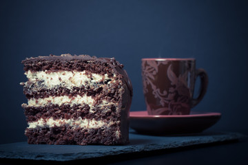 A piece of chocolate cake and cup of coffee on slate plate on bl