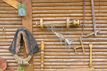 Old rural utensils hang on log wall. 
