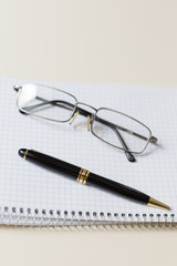 black pen and glasses with white pad or notepad