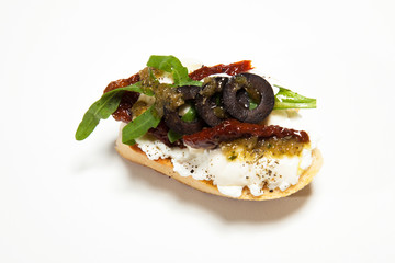 Sandwich with white cheese, dried tomato, olives and arugula on