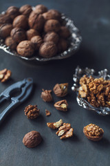Walnuts in a bowl, whole and chopped on grey wooden table. Vintage style