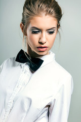 Beautiful young woman wearing a shirt and bow tie against a gray background