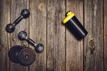 Old iron dumbbells and shaker on an old wooden table. Image taken from above, top view
