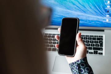 Eine Frau hält ein Smartphone über einem Notebook in den Händen