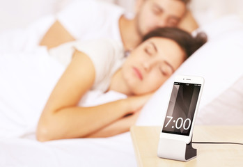 Obraz na płótnie Canvas Happy couple waking up with mobile alarm clock