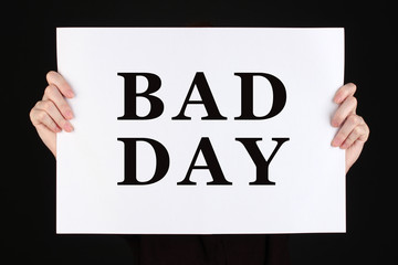 Woman holding poster with text Bad Day in front of her face isolated on black