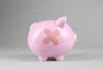 Piggy Bank with adhesive bandage on grey background