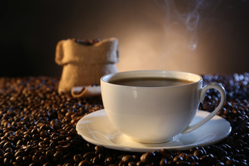 Cup of hot coffee among coffee beans on dark background