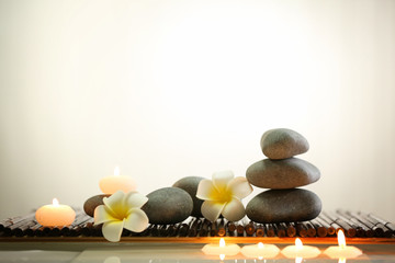 Spa still life with stones, candles and flowers in water on light background