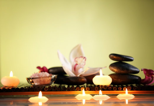 Spa still life with stones, candles and flowers in water on green blurred background